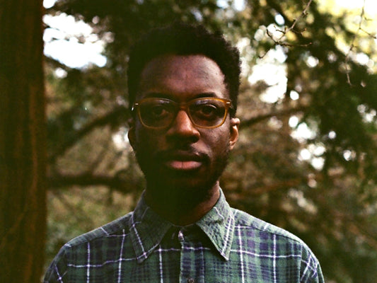 Matthew Gordon with short black afro hair, wearing brown glassess and a blue/green plaid shirt